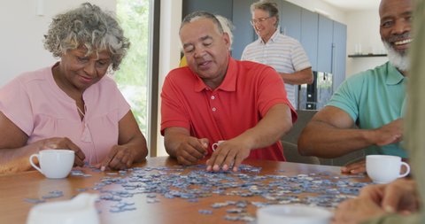 Happy senior diverse people playing puzzle at table at retirement home. healthy, active retirement and body inclusivity.