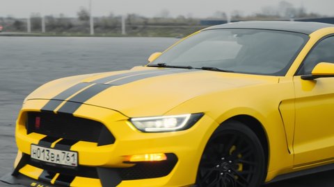 Yellow Ford Mustang with black stripes. Slowly driving through the parking lot in the evening. 50FPS. Russia, Rostov-on-Don 23oct2021
