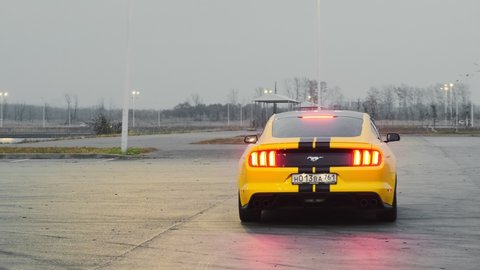 Yellow Ford Mustang with black stripes. It stands in the parking lot and slowly drives off. Slow motion. Russia, Rostov-on-Don 23oct2021
