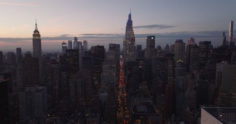 Forwards fly above city at dusk. Illuminated iconic high rise buildings Chrysler and Empire State Building. Manhattan, New York City, USA in 2021