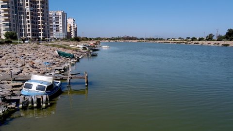 The Segura River flows to the ocean on the coast of Spain with old and sunken boats along the shore by apartment buildings