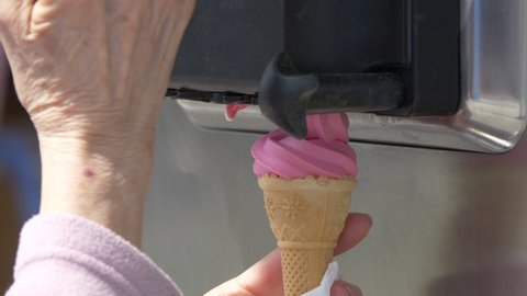 Super slow motion shot of female ice-cream vendor preparing pink soft ice cream in summer