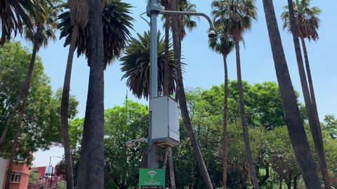 Mexico City , Mexico - 05 13 2022: Free WIFI Sign On Lamppost In Mexico City Park With Traffic Going Past In background Seen Through Trees. Tilt Down