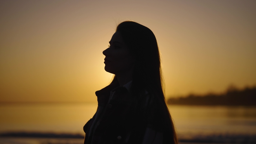 Silhouette portrait of a young woman at sunset. Inspiration and search for harmony in the evening alone.