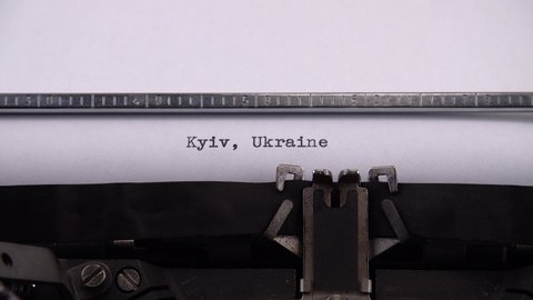 Typing name of Ukrainian city and capital of Ukraine "Kyiv, Ukraine" on retro typewriter.