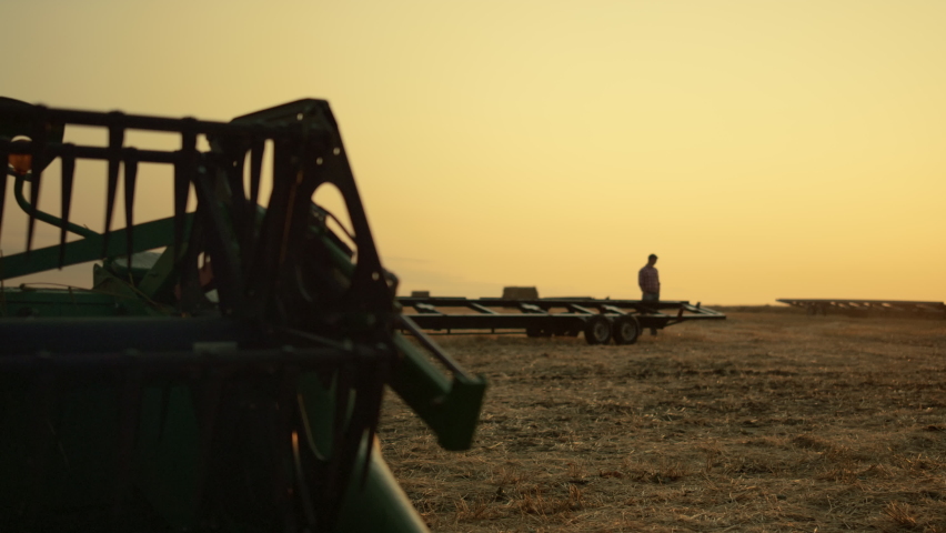 Farmer silhouette at wheat field harvesting equipment at golden sunset time. Unknown agrarian agribusiness owner standing on cereal farmland inspecting cropping machinery working day end. Agro concept | Shutterstock HD Video #1090441763