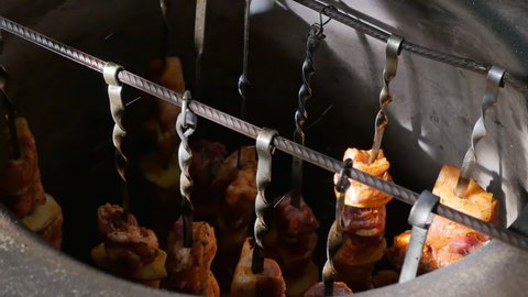 the fingers of a kebab man move skewers with Armenian khorovats along the crossbar in a hot tonir with a cloth rag due to the hot temperature. National meat skewers