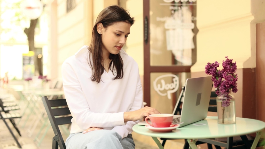 Portrait of attractive woman using laptop in coworking space or cafe. Young woman sitting in front open laptop computer and looking ahead. Study, learning, remote work, freelance.