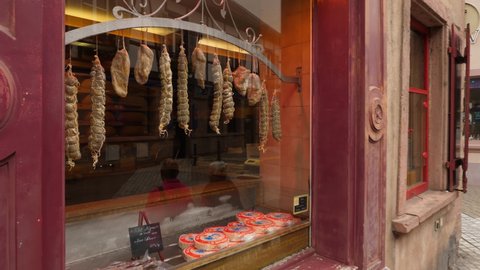 RIBEAUVILLE, FRANCE - AUGUST 20, 2019: Camera move to butcher store window and show dry-cured sausages hanging behind glass. Boucherie Traiteur Charcuterie at Ribeauville town, cosy food store