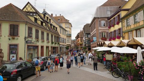 RIBEAUVILLE, FRANCE - AUGUST 20, 2019: Charming little town at Alsace, unidentified people walk at main street, old buildings around. Clothing stores and souvenir shops, restaurant terrace on the way