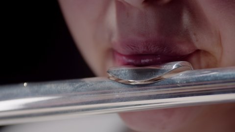 Female musician plays flute in studio with dark background, closeup lips. Closeup female lips of musician playing flute in studio