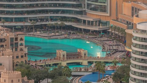 Shopping mall exterior with reataurants near fountain in Dubai downtown aerial timelapse, United Arab Emirates. Bridge over lake and walking area at evening