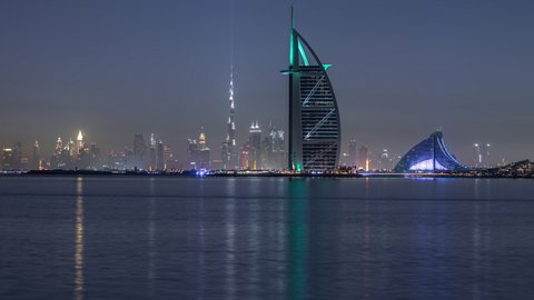 DUBAI, UAE - CIRCA APRIL 2021: Skyline of Dubai by night with Burj Al Arab from the Palm Jumeirah panoramic timelapse. Illuminated skyscrapers reflected in water