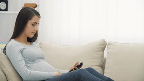4k slow motion video of pregnant woman on the sofa taking selfie.
