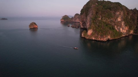 wide aerial circling a single thai longtail boat during sunrise near Railay Beach in Krabi Thailand around the beautiful limestone mountains of Krabi Thailand in the Andaman Sea