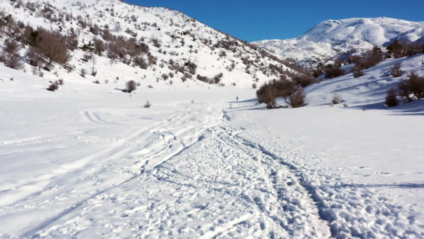 Man in khaki-colored hiking pants and black polo does Nordic walking in his mountain boots in a thick layer of snow in Mount Hermon in Israel on a sunny day. Aerial steady shot with vertigo affect