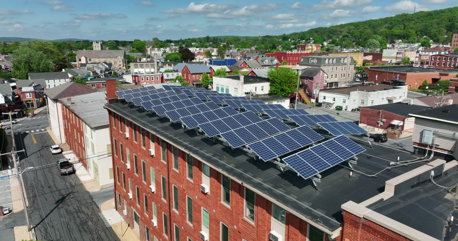 Aerial flyover of solar panels on top of roof. Small town America uses renewable energies to power grid. Energy of the future theme.