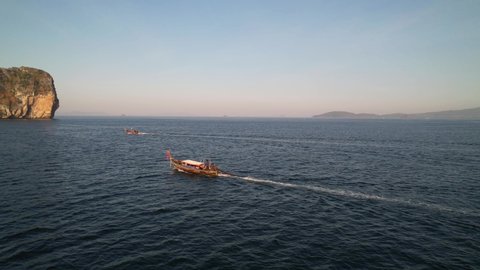 aerial drone flying parallel with two thai longtail boats during sunrise in the Andaman Sea with large limestone rocks in the distance in Krabi Thailand.