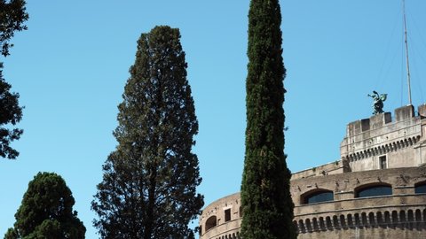 Rome, Italy - July 24, 2019: View of the fortress of Castel Sant'Angelo, from the park below through cypress trees. with bronze angel statue by Peter Anton von Verschaffelt
