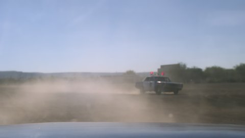 Old police cars in a high speed pursuit, driving zig zags in a dramatic way raising clouds of dust