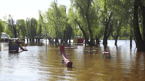 Flooded children playground in public city park near beach of river. Landscape of Ukraine, Europe. Overflow of level of water in river during springtime season. Seasonal natural disaster and damages