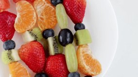 Fresh fruit skewers on a plate for a healthy snack on a white background. Rotate video.