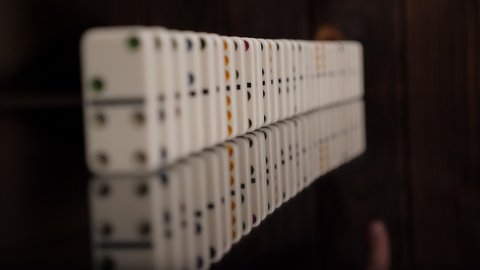White domino dice slowly fall on a black mirror surface. Domino effect. Concept of domino effect and chain reaction. The background is blurred.