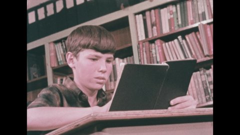 1960s: Boy holds book, touches page, looks nervous. Librarian sits at desk, talks to boy, points to card catalog. Boy sits at desk, closes book, looks around. Boy pulls at torn page.