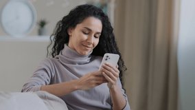 Young female attractive arabian muslim girl woman in hijab sit on sofa smiling islamic lady texting message on smartphone with boyfriend work with mobile digital app shopping online search information - Powered by Shutterstock - Get 15% off with code: PIKWIZARD15