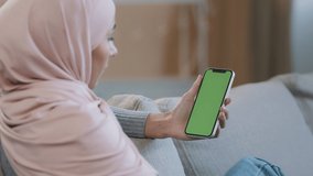 Over shoulder business woman islamic arabian girl in hijab sit on cozy sofa at home hold mobile in hand with green screen chroma key display watching online video news use social app service website - Powered by Shutterstock - Get 15% off with code: PIKWIZARD15