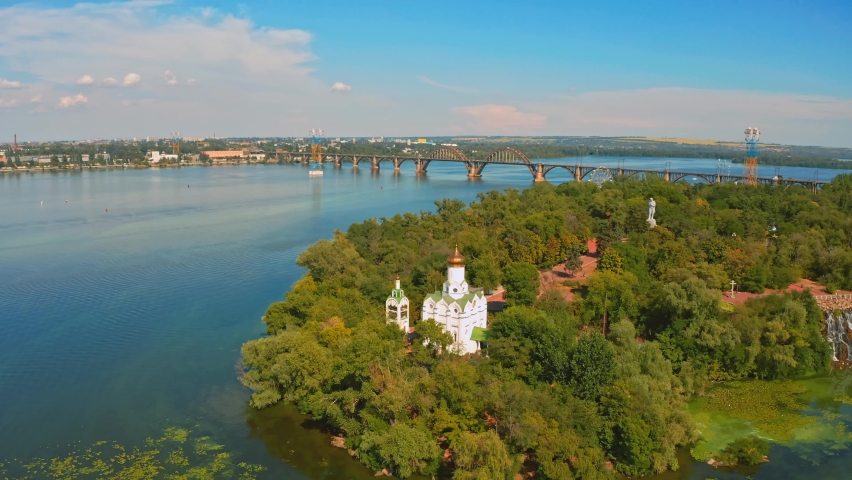 Aerial view over beautiful white church on island surrounding by river - while sunset.  Drone flying above old church on a green island with river. Ukraine, Dnepr city. 2020 year. Royalty-Free Stock Footage #1090481515