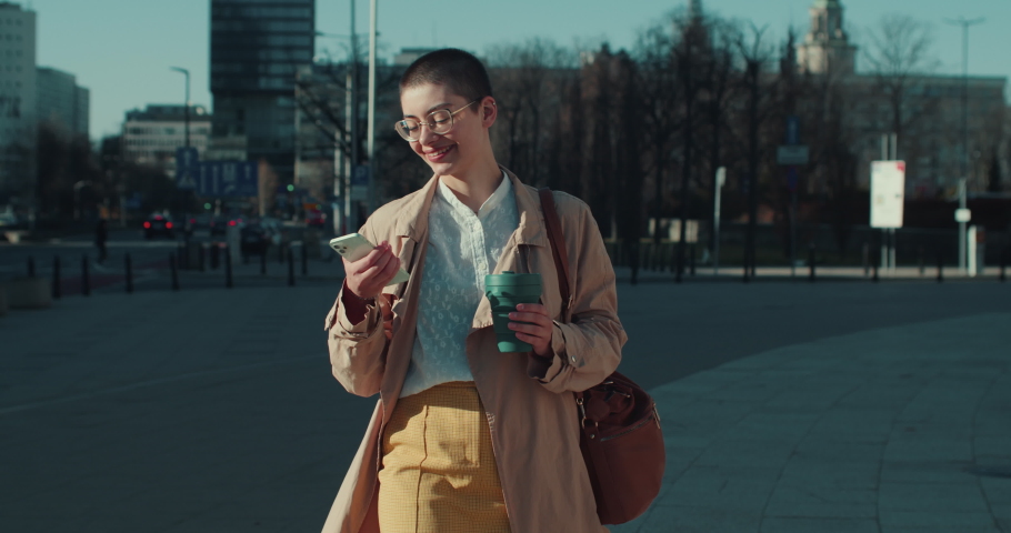 Tilt down on happy beautiful young short haired blogger woman using phone app on the move in sunny street slow motion.