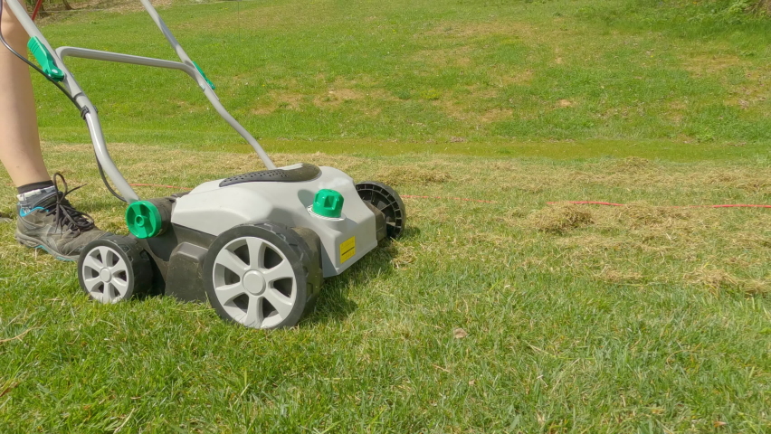 SLOW MOTION: Young woman using lawn aerator to grow healthier and thicker lawn. Spring backyard garden work for lawn growth enhancement. Practical gardening machinery for efficiency at landscaping. | Shutterstock HD Video #1090484205