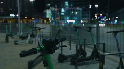 Electric scooters in the night city. Ecological. Electric scooters are parked in the center of the night city.  In the background, night city lights and on the road, cars with their headlights on.
