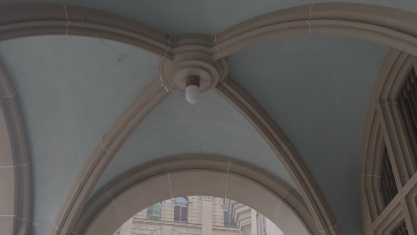 Concrete vaults, blue wall background. Light bulb in the center of the beams. The movement of the ceiling vaults in the arch of the old building, exit to the square to the tower. Bright light. | Shutterstock HD Video #1090497027