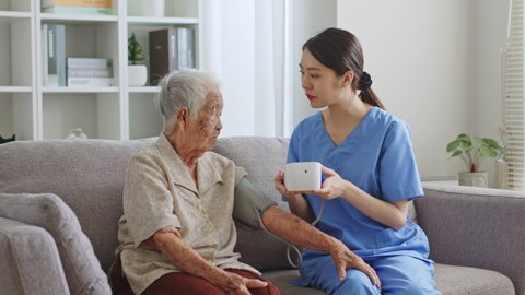 Young Asian woman, nurse, caregiver, carer of nursing home checking blood pressure measurement with senior Asian woman at home, nursing home concept