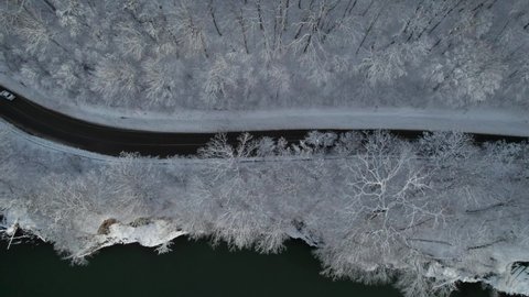 Aerial top down cinematic winter snow cowered country road, asphalt serpentine. Cars go traffic among forest.