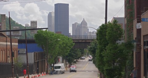A long shot view of the iconic Pittsburgh skyline as seen from Butler Street in Lawrenceville. Traffic passes under a railroad bridge in the foreground.  	