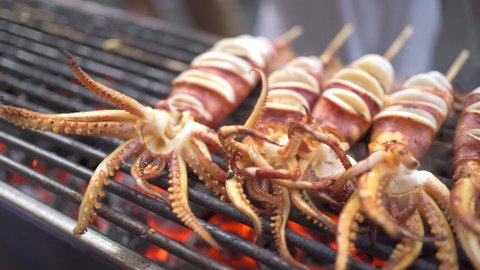4K footage showing an Asian street food in Bangkok - Thailand. Unrecognizable man grilling a squid or seafood barbecue on the charcoal fire wood.