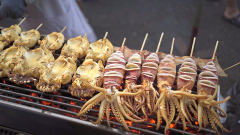 4K footage showing an Asian street food in Bangkok - Thailand. Unrecognizable man grilling a squid or seafood barbecue on the charcoal fire wood.