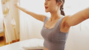 Young Asian woman is exercising yoga at home. Fitness, workout, healthy living and diet concept. Female watching videos online on laptop computer in bedroom.