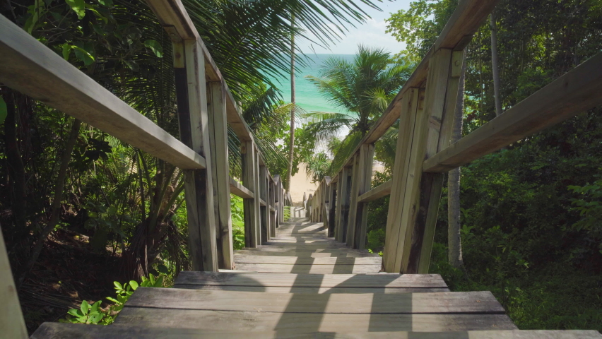 Scenic view person walking barefoot wooden boardwalk sea sunny palms background island. Footprints POV steps leading stairs coconut seaside tropical summer holiday vacation concept 2022. Australia