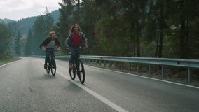 Lovers cycle mountain bikes on nature road. Happy couple enjoy sport activity. Smiling travelers ride fast on forest highway. Smiling tourists training on bicycles in summer landscape. Leisure concept - Powered by Shutterstock - Get 15% off with code: PIKWIZARD15