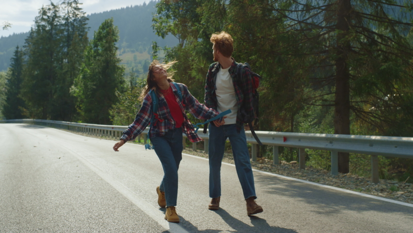 Happy walkers enjoy hitchhike in summer mountains. Carefree hikers trekking on road highway. Positive friends show thumbs up on weekend travel. Couple tourists go together in forest. Holiday concept. Royalty-Free Stock Footage #1090508883