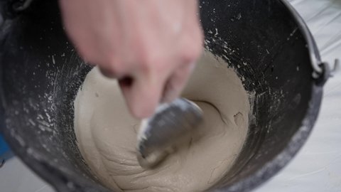The tile grout is mixed with a spatula. Stirs cement or mortar mixed with water, top view and close-up. Mixed mortar cement in container ready to be used.