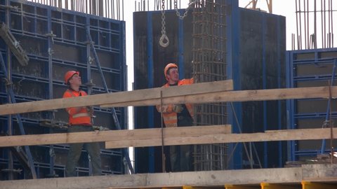 Ukraine, Kiev. 24.04.2019: Construction worker climbing on the metal frame. Two builders wearing orange clothing.