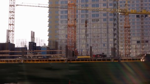 Kyiv,Ukraine - 24.04.2019: Crane lifts up metal frame on the construction site. Worker wearing orange vest and helmet.