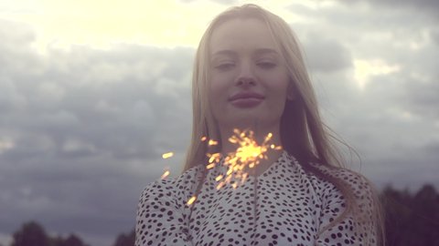 Beauty model girl holding Bright burning sparkle in darkness closeup. Beautiful woman with sparklers celebrating, outdoors. Sparklers holiday backdrop. 4K slow motion