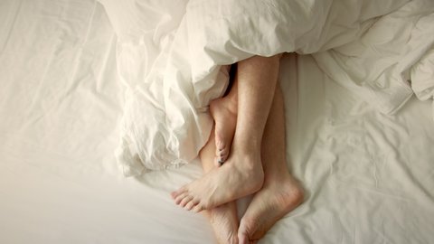 Couple petting in bed. Marriage, family, love. Only feet in frame. Marriage, family, love, sex concept. Male and female legs, top view, white underwear.