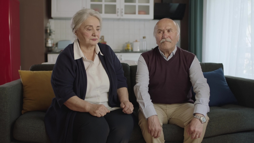 Mature elderly couple sitting on sofa in living room. The old couple who just had a fight, sitting quietly without talking to each other. Problem concept in the marriage of the elderly.